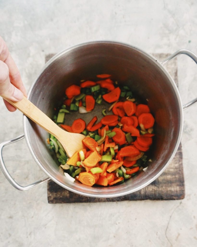 vegetable consomme ingredients sauteing in a stock pot