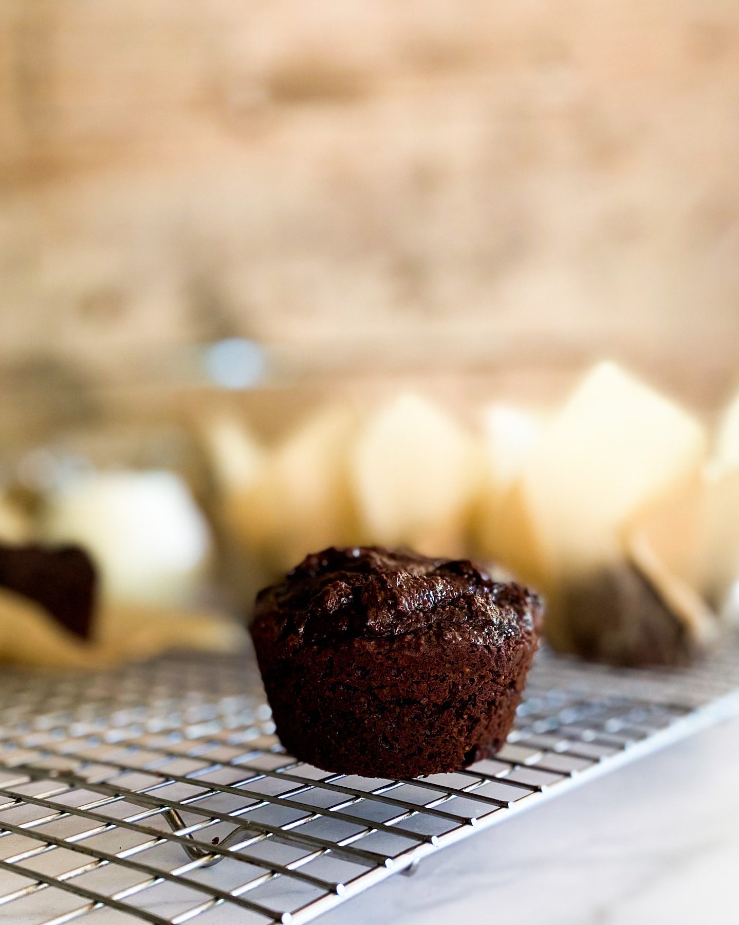 Brownie muffins on a cooling rack with many muffins in its wrapper in the background