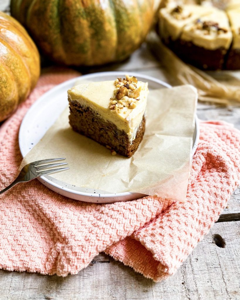 a slice of pumpkin carrot cake with pumpkins in the back