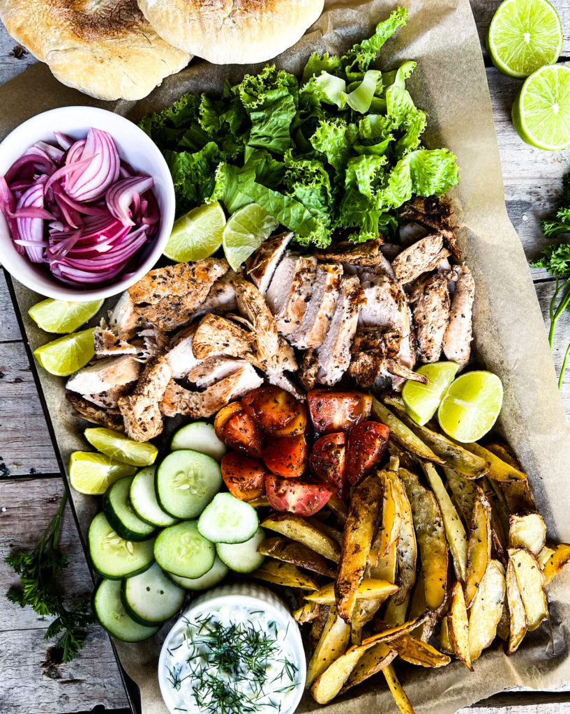 A bake tray of lemon marinated chicken pitas with oven baked fries and toppings