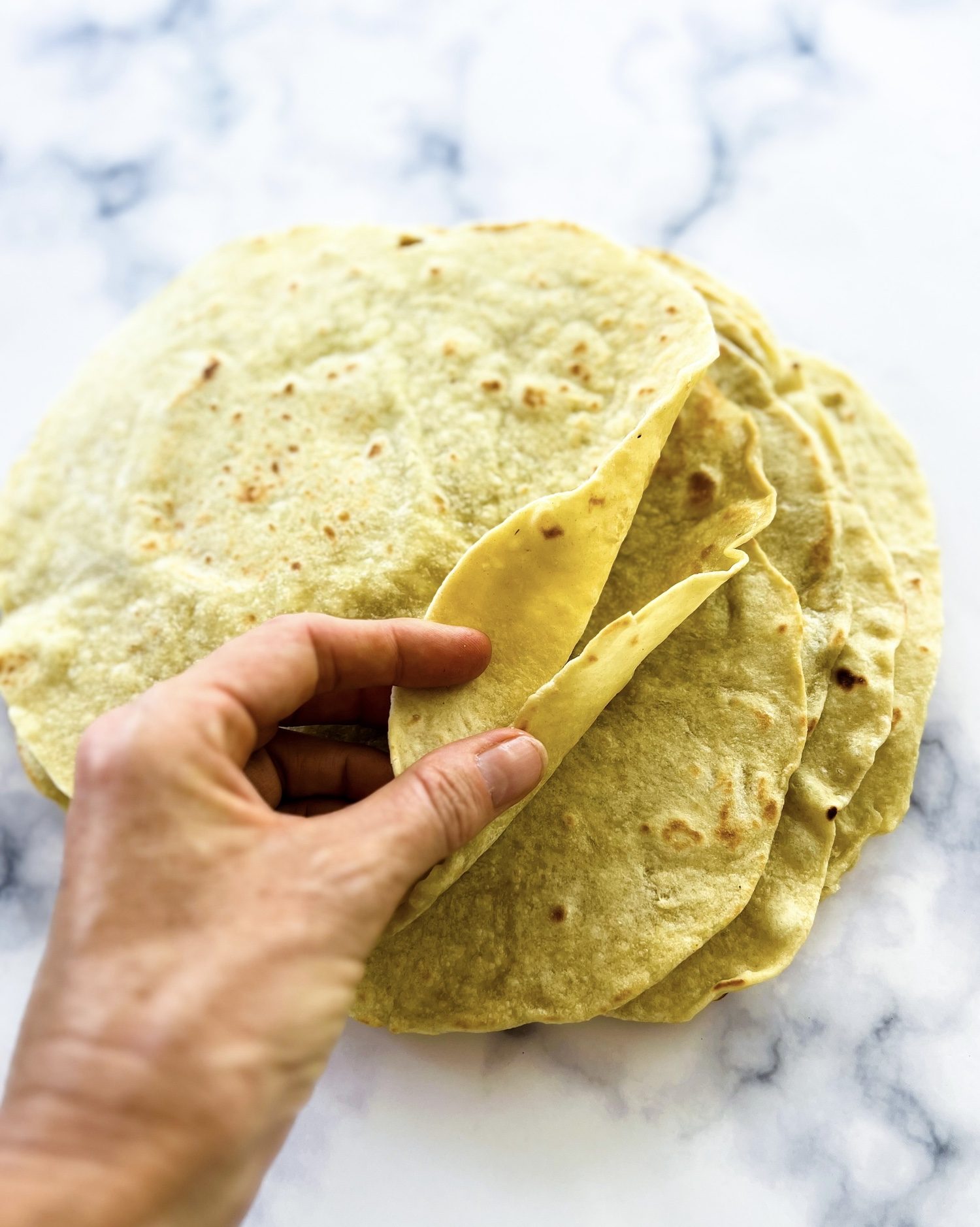 a hand going through a stack of fresh whole wheat tortillas