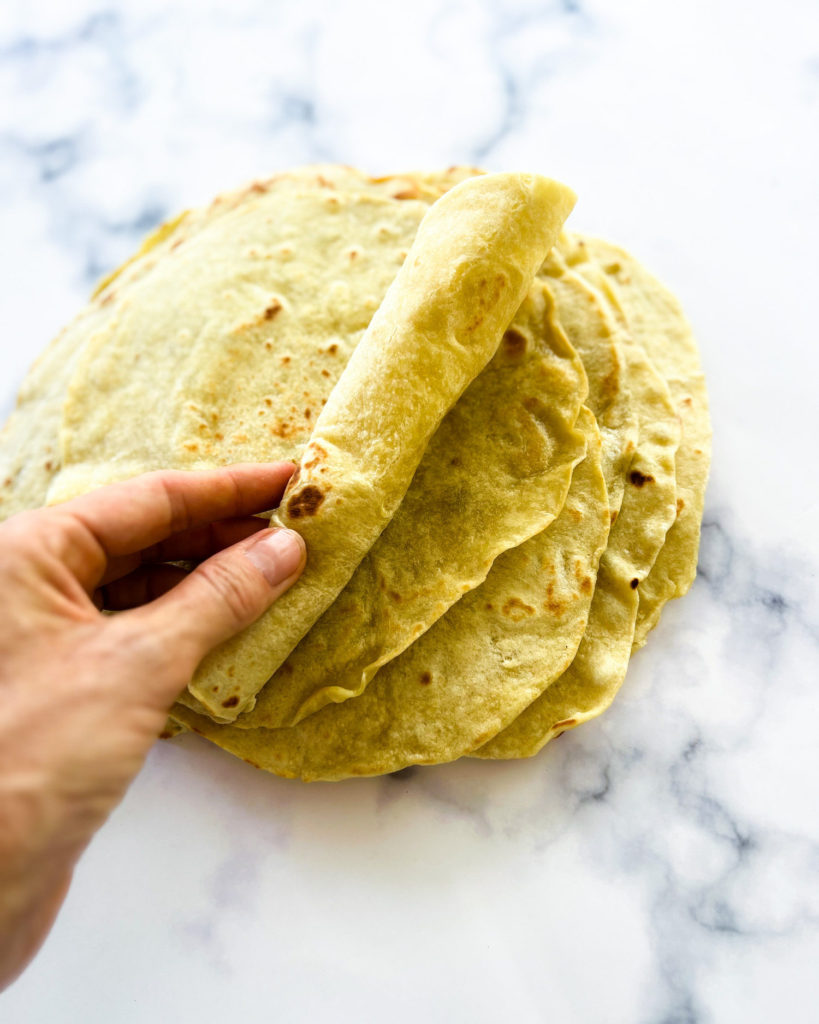 a hand rolling up a tortilla from a stack