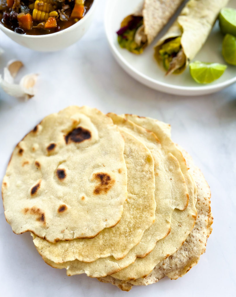 a stack of tortillas and a plate of 2 filled and rolled up tortillas