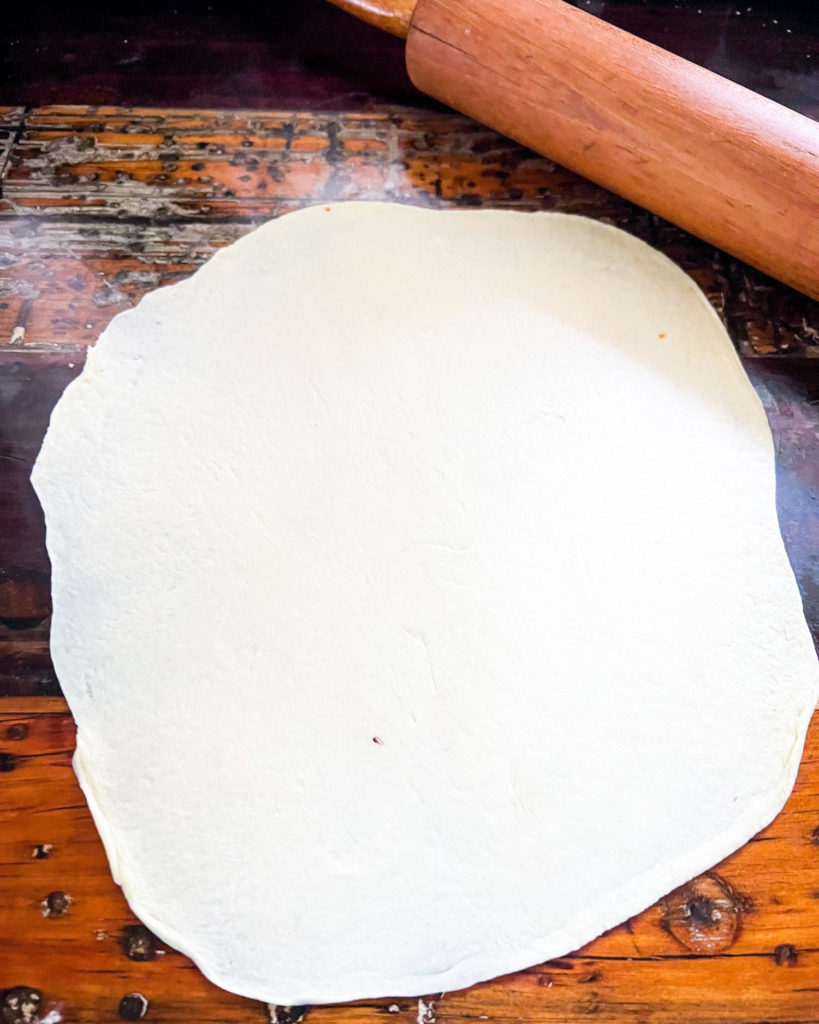 a rolled out tortilla next to a rolling pin on a kitchen countertop