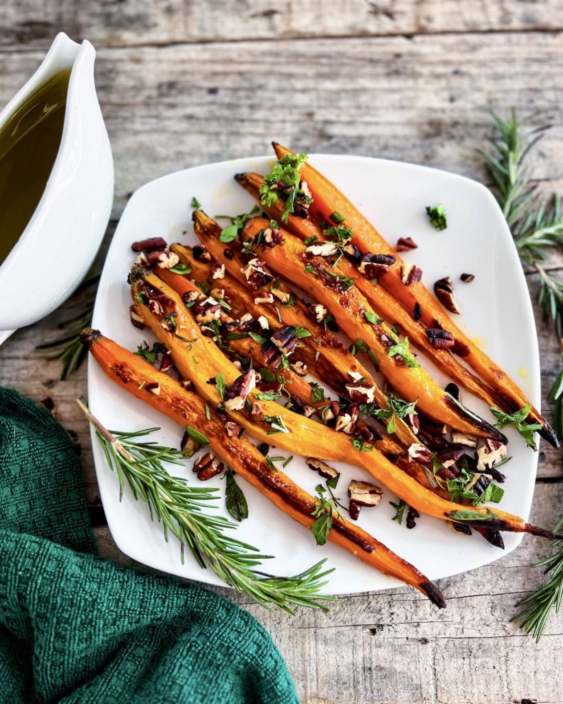 Roasted carrots on a plate topped with pecan herb crumble and maple glaze on the side