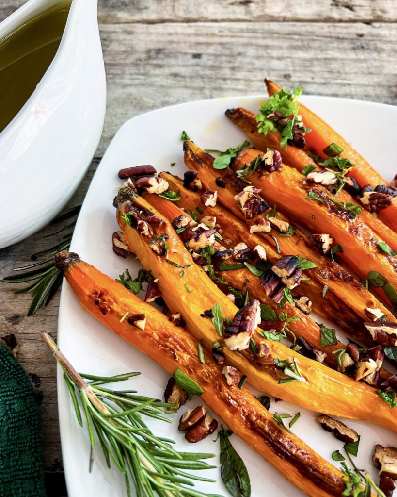Roasted carrots on a plate topped with pecan herb crumble and maple glaze on the side close up
