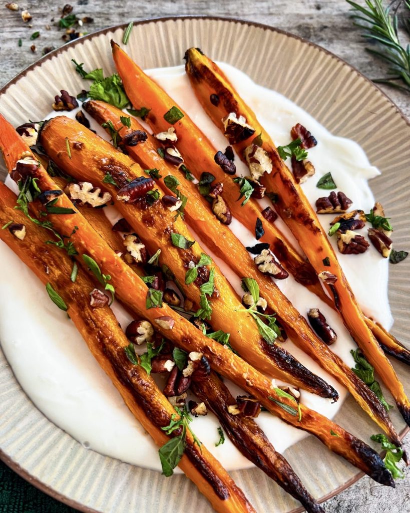 Close up of roasted carrots on whipped ricotta topped with pecan herb crumble and maple glaze on the side
